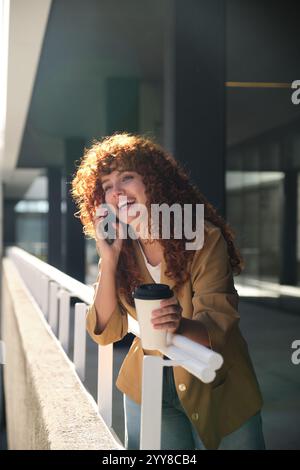 Happy businesswoman talking on phone and drinking coffee during break Stock Photo
