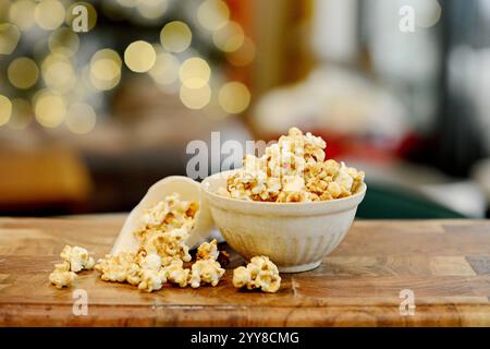 Caramel popcorn in a bowl with festive lights on wooden table. Stock Photo