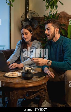 Two young adults collaborating on a project while discussing ideas in a relaxed indoor setting. The scene includes a laptop, tea, and snacks, symboliz Stock Photo