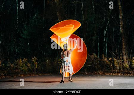 Woman posing at night with glowing orange spiral light art Stock Photo