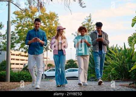 Friends enjoying a casual stroll while using smartphones in a park Stock Photo
