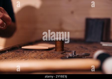Spool of brown thread on a leatherwork artisan’s wooden table Stock Photo