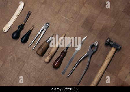 Leather crafting tools neatly arranged on wooden workbench Stock Photo