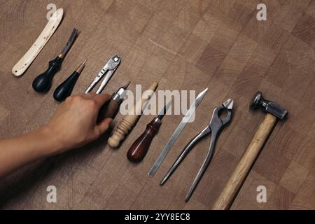 Artisan hand organizing leatherworking tools on wooden table Stock Photo