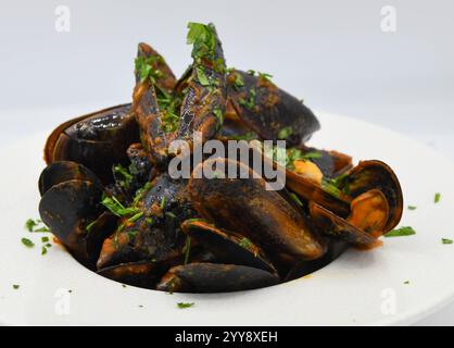 Mussels cooked in a pan with parsley on a white background. Stock Photo