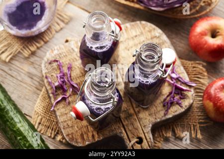Purple cabbage juice in three glass bottles with red apples and cucumber Stock Photo