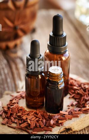 Three brown dropper bottles of aromatherapy essential oil on a table with red sandalwood chips Stock Photo