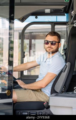 Vertical portrait of male bus driver in sunglasses on bus stop in city. Stock Photo