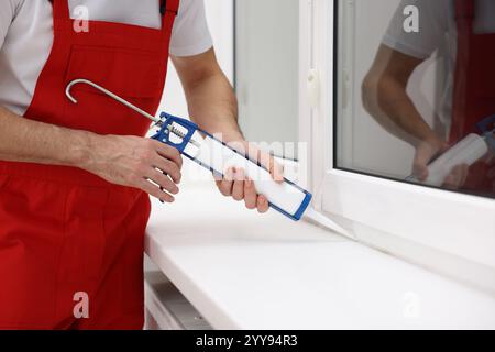 Worker with caulking gun sealing window indoors, closeup Stock Photo