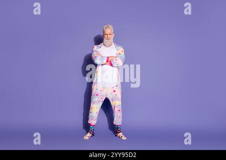 Stylish man in unicorn pajamas stands confidently against a purple background Stock Photo