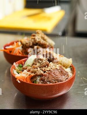A vibrant bowl of Vietnamese bún thịt nướng featuring grilled pork, crispy spring rolls, vermicelli noodles, pickled carrots and daikon, fresh herbs, Stock Photo