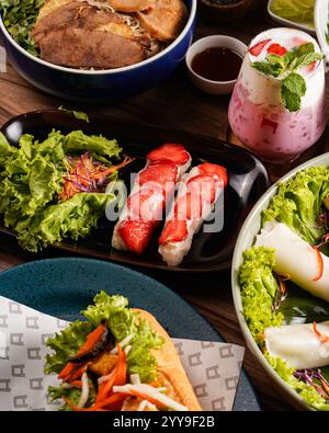 Assorted Vietnamese cuisine featuring strawberry fresh spring rolls, grilled meat vermicelli bowl, bánh mì sandwich, steamed rice rolls, and a refresh Stock Photo