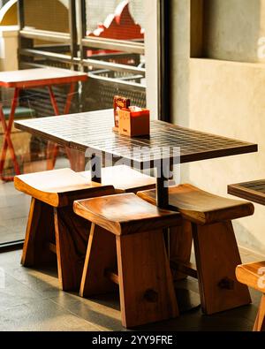 Empty wooden table and stools in a modern café interior with warm sunlight streaming through the window. Stock Photo