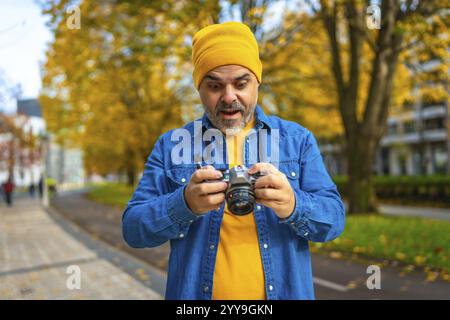 Mature man tourist checking the pictures on the screen of a camera while photographing the city during autumn Stock Photo