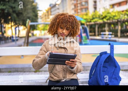 Latin beauty female student using digital tablet sitting on an urban park bench in the city Stock Photo