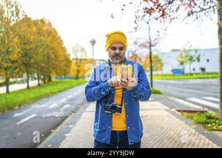 Modern mature man with camera holding from neck using phone while visiting a city Stock Photo