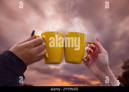 closeup of a toast between two yellow cups held aloft by two female hands with well-manicured nails Stock Photo