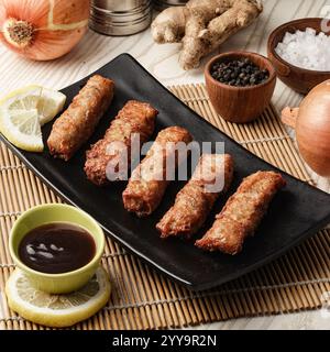 Delicious crispy spring rolls served on a black plate with soy-based dipping sauce, garnished with lemon slices and surrounded by fresh ingredients Stock Photo
