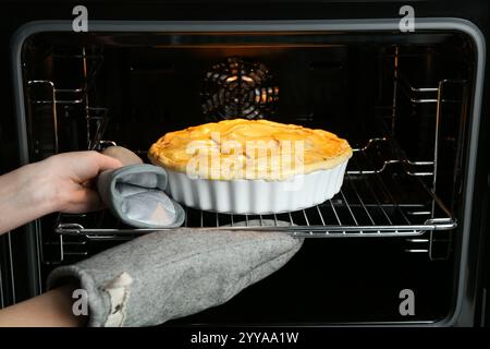 Woman putting homemade apple pie into oven in kitchen, closeup Stock Photo