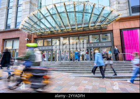 Motion blurred ebike speeding and passing shoppers at the entrance to Buchanan Galleries Shopping Centre, Buchanan Street, Glasgow, Scotland UK Europe Stock Photo