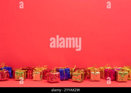 A vibrant display of small, colorful gift boxes tied with gold ribbons, set against a bright red background. holiday gift, and special occasions. Stock Photo