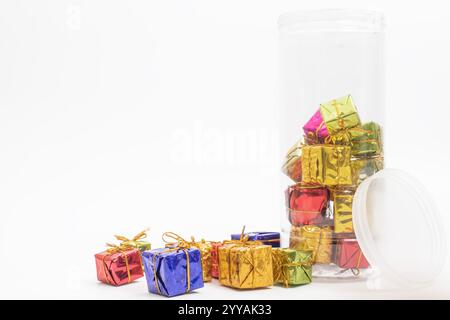 Colorful miniature gift boxes placed inside a clear plastic jar, lying on its side against a white background. perfect for holiday gift decor. Stock Photo