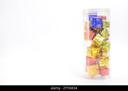 A pile of small, colorful gift boxes wrapped in shiny paper and arranged in a clear container, set against a vibrant white background. Perfect for hol Stock Photo