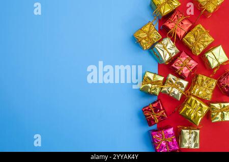 A variety of shiny wrapped gift boxes with ribbons are arranged on a vibrant red and blue surface. festive and decorative holiday. Stock Photo