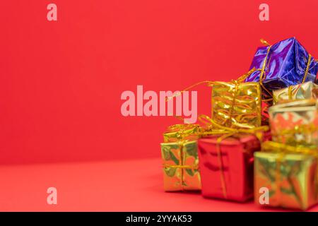 A vibrant arrangement of small gift boxes in gold, red, and blue, elegantly decorated with golden ribbons, set against a red surface. perfect for holi Stock Photo