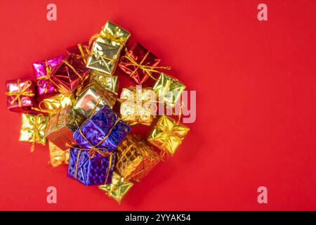 Multicolored gift boxes adorned with golden bows, beautifully scattered on a bright red background. perfect for holiday, birthday, or special occasion Stock Photo