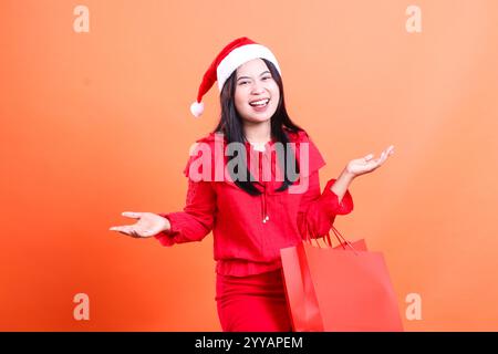 gesture of beautiful ladies wearing red christmas blouse, Santa hat, cheerful looking forward both hands offering to the side and carrying red bag of Stock Photo