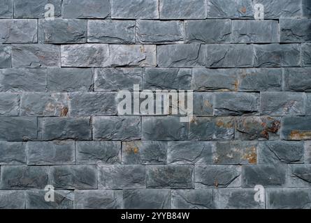 A brick wall with a grey color. The wall is made of bricks. The bricks are of different sizes Stock Photo