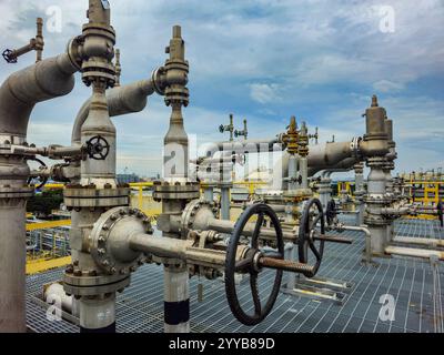 A large group of valves and pipes are on a platform. The valves are black and the pipes are silver Stock Photo