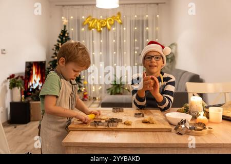 Two cheerful boys in Santa hats making Christmas cookies together in a beautifully decorated kitchen  Stock Photo