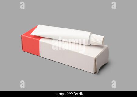 small white tube on cardboard box isolated gray background, mockup template container of ointment, cream, toothpaste, gel or shampoo, blank package Stock Photo