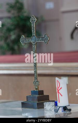 A small cross is on a table next to a candle. The candle is lit and has a red cross on it Stock Photo