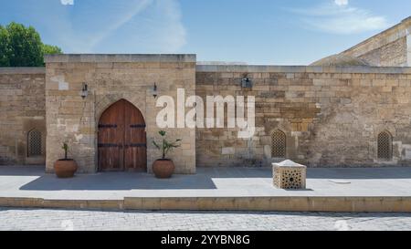 A sunlit courtyard showcases ancient stone walls and a beautifully carved arched wooden door. Decorative planters and intricate lattice windows enhance the historical atmosphere Stock Photo