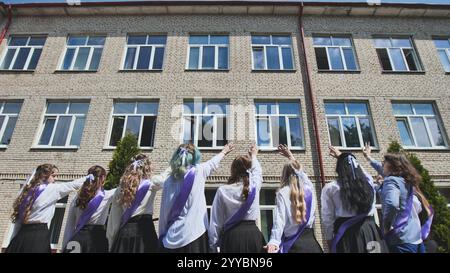 Group of graduating female students waving goodbye to their school building on their last day, celebrating the end of an era Stock Photo