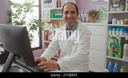 A mature hispanic man in a white lab coat works on a computer in a pharmacy with shelves of products in the background. Stock Photo