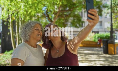 Two mature women taking a selfie together in an outdoor setting, enjoying a pleasant moment under the trees Stock Photo