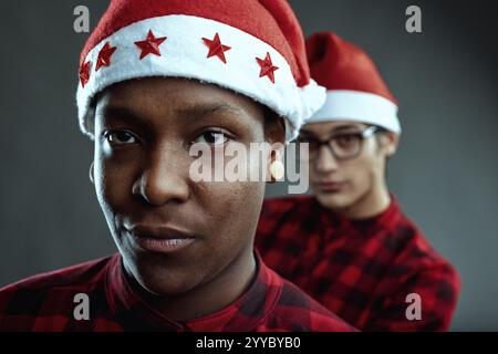 Two diverse young adults wearing matching red and black checkered shirts and santa claus hats looking at the camera with a serious expression Stock Photo