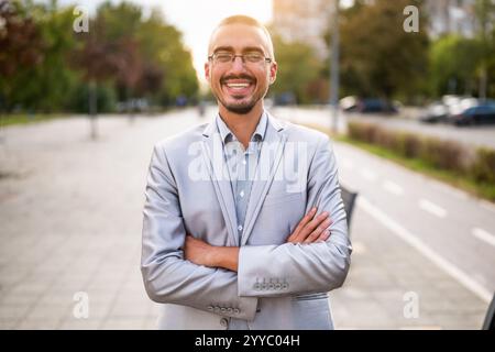 Portrait of cheerful young businessman who is standing in the street, looking at camera and smiling. Stock Photo
