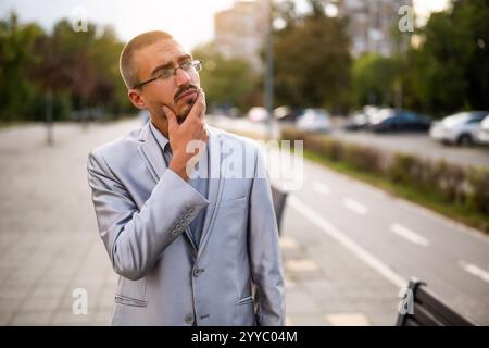 Portrait of thoughtful and worried young businessman who is standing in the street and looking away. Stock Photo