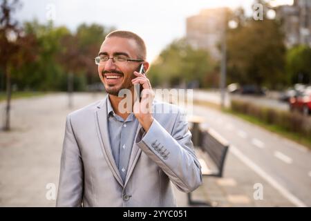 Portrait of cheerful businessman who is talking on phone. Young businessman standing in the street and using smartphone. Stock Photo