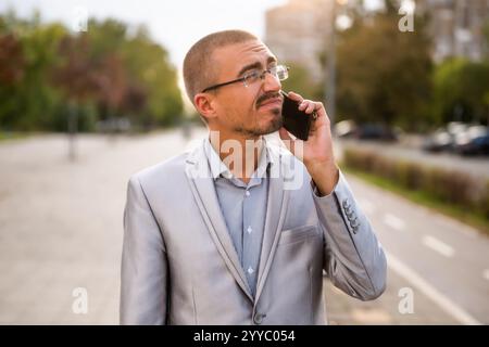 Portrait of distraught businessman who is talking on phone. Young businessman standing in the street and using smartphone. Stock Photo