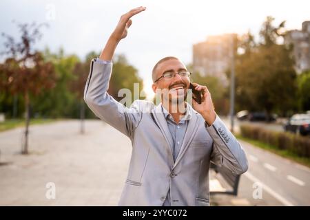 Portrait of cheerful businessman who is talking on phone. Young businessman standing in the street and using smartphone. Stock Photo