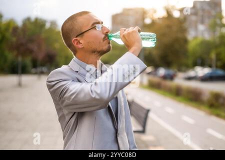Portrait of young businessman who is standing in the street and drinking water. Stock Photo