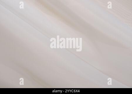 A soft beige fabric is gently draped across a smooth surface, illuminated by natural light. The subtle texture and tones create a calming atmosphere, Stock Photo