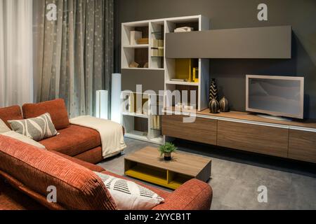 Stylish modern living room featuring a comfortable red sofa, a large tv, and contemporary furniture, creating a cozy and inviting atmosphere Stock Photo