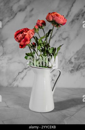 Bouquet of artificial red roses in a white steel milk jug vase. Grey background. Stock Photo
